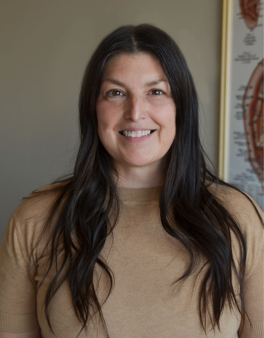 Headshot of acupuncturist Kelly Nichols in a cream shirt and acupuncture sign behind her