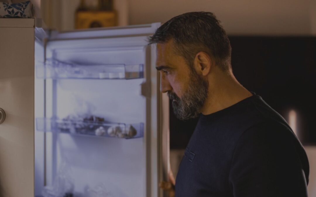 Man looking into his home's refrigerator at night to find something to eat.